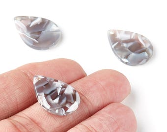 May include: Three teardrop-shaped beads with a marbled pattern of gray and white. One bead is held in a hand, while the other two are on a white surface. The beads have a glossy finish and a hole at the top for stringing.