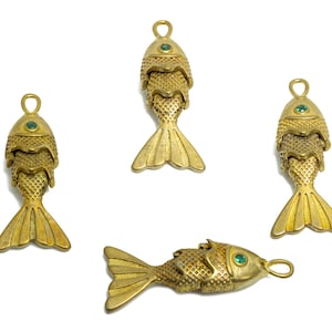 May include: Four gold-colored fish charms with green gem eyes. The charms are layered and have a detailed, textured finish.