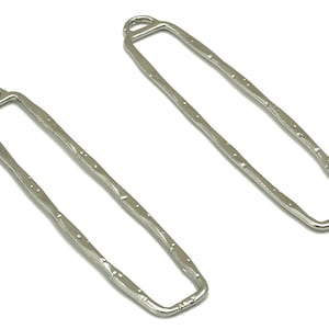 Pode incluir: Dois pendentes retangulares de metal prateado com superfície texturizada e um laço na parte superior.