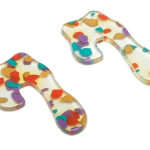 May include: Two clear plastic earrings shaped like a sideways U with a colorful confetti pattern. The confetti is in shades of orange, red, purple, and teal.
