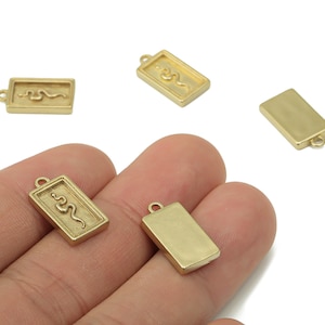 May include: Gold-coloured rectangular charms with a snake design. The charms have a loop at the top for attaching to jewellery. One charm is blank. The charms are small, suitable for necklaces or bracelets.