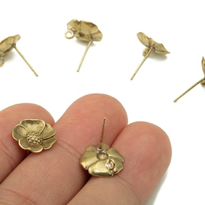 Peut inclure: Boucles d'oreilles à clous en forme de fleur de couleur or. Les boucles d'oreilles présentent un motif floral détaillé avec une tige et une petite boucle pour l'attache à l'oreille. L'image montre plusieurs boucles d'oreilles.