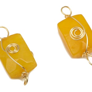 Puede incluir: Dos colgantes de piedra amarilla con alambre dorado envuelto alrededor. El alambre está retorcido en forma de espiral.