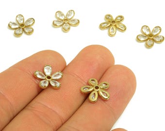 May include: Close-up of several gold-colored flower-shaped charms. Some charms have clear, sparkling accents. Two charms are held in a hand. The charms are likely for jewelry making or craft projects.