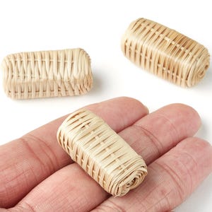 Könnte beinhalten: Drei kleine, gewebte Rattanobjekte. Eines wird in einer Hand gehalten, während die anderen beiden sich auf weißem Hintergrund befinden. Die Objekte sind rechteckig und zylindrisch, hellbraun und mit einem Korbgeflechtmuster.