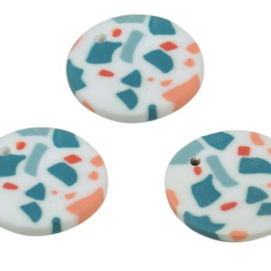May include: Three round white ceramic ornaments with a hole in the centre. The ornaments are decorated with a terrazzo pattern in shades of teal, light blue, and peach.