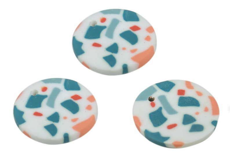 May include: Three round white ceramic ornaments with a hole in the centre. The ornaments are decorated with a terrazzo pattern in shades of teal, light blue, and peach.