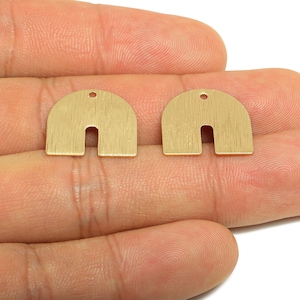 May include: Two gold-colored, half-circle shaped metal earring components with a U-shaped cutout at the bottom. Each component has a small hole at the top for attachment. The components are held in a hand.