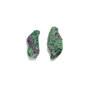 May include: Two raw, unpolished mineral specimens featuring a vibrant green matrix speckled with deep magenta and purple crystalline inclusions. These irregular, jagged stones display a rough, natural texture with contrasting color variations.