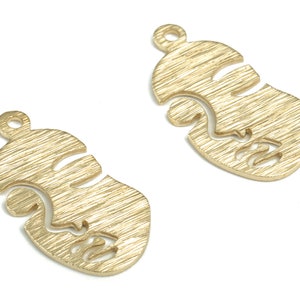 Puede incluir: Dos abalorios de metal de color dorado en forma de rostro estilizado con una superficie texturizada.