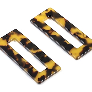 Può includere: Due fermagli per capelli rettangolari marroni e gialli con un foro rettangolare al centro. I fermagli hanno un motivo a tartaruga.