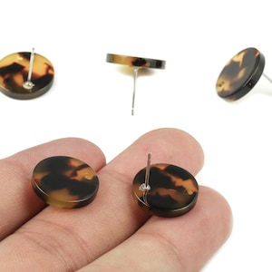 May include: Round stud earrings with a tortoiseshell pattern. The earrings are brown and tan with a post backing. Several earrings are shown, some lying flat and others at an angle.