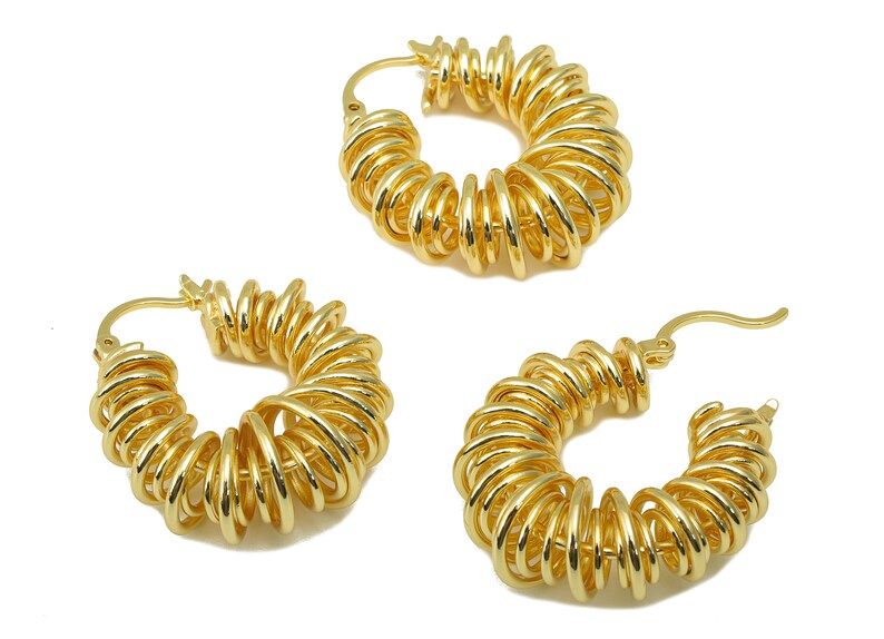May include: Three gold-colored hoop earrings. Each earring features a spiral design, with multiple loops creating a textured, eye-catching appearance. The earrings are displayed against a white background, highlighting their metallic sheen.