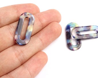 May include: Two oval-shaped acrylic beads with a marbled pattern in shades of blue, purple, and yellow. One bead is held in a hand, while the other is connected to a second bead. Each bead has a small hole.