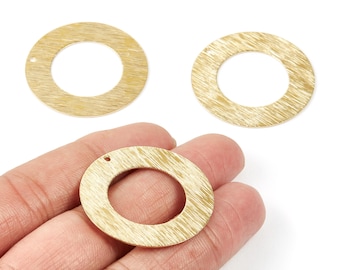 May include: Three gold-coloured, circular jewellery components with a textured, brushed finish. One is held in a hand, and the other two are on a white background. Each has a small hole for attachment.