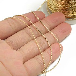 May include: Gold-coloured braided cord, wound around a spool, with a few loops of the cord laid out on a hand.