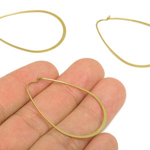 Puede incluir: Pendientes de aro dorados en forma de lágrima. Los pendientes tienen un diseño sencillo y elegante con un acabado liso y pulido. Los aros son ligeros y adecuados para el uso diario. Fondo blanco.