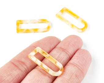 May include: Three open-ended, rectangular resin charms with a marbled yellow and cream pattern. One charm is held in a hand, while the other two are scattered on a white background. These charms are suitable for jewelry making.