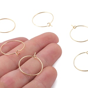 May include: Several gold-colored hoop earring findings are displayed. The open hoops vary in size and have a simple, minimalist design. The findings are shown against a neutral background, highlighting their metallic sheen. These are ideal for jewelry making.