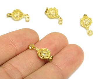 Puede incluir: Colgante dorado con diseño geométrico. El colgante tiene una estructura similar a una jaula con una pequeña gema cuadrada en el centro. Un pequeño dije cuadrado cuelga debajo.