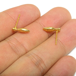 May include: A pair of gold-colored stud earrings. Each earring features a small, stylized fish design. The earrings are shown against a neutral background, highlighting their metallic sheen and intricate details. These earrings are suitable for everyday wear.