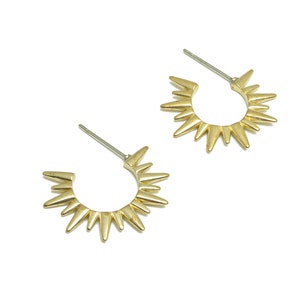 May include: A pair of gold-toned hoop earrings with a sunburst design. The earrings have a pointed, starburst shape.