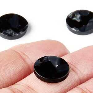 May include: Three black and white marbled round beads. One bead is held in a hand, showing a hole for stringing. The other two beads are on a white background. These beads are suitable for jewelry making.