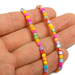 Op de afbeelding: Close-up van twee strengen kleurrijke vierkante kralen in verschillende kleuren, waaronder roze, geel, oranje, groen en blauw. De kralen zijn aan elkaar geregen en creëren een levendig en speels accessoire.