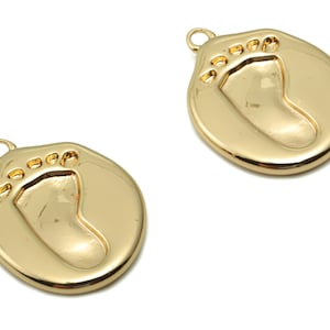 May include: Two gold-tone metal charms shaped like a baby's footprint. Each charm has a loop at the top for attaching to a necklace or bracelet.