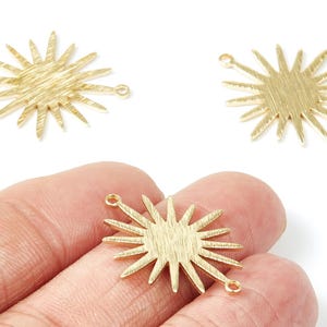 Peut inclure: Charm en forme d'éclat de soleil doré avec des surfaces texturées et de petites boucles à chaque extrémité. Vue rapprochée, dont un est tenu dans une main. Le motif en forme d'éclat de soleil présente des rayons pointus.