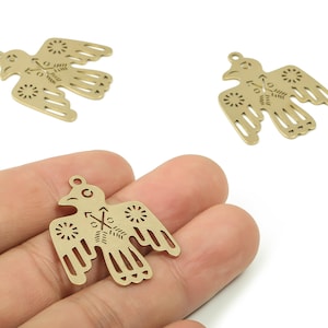 May include: Gold-colored metal bird charms with intricate cut-out designs. The charms feature a bird silhouette with detailed wings and a small loop for attaching to jewelry or other crafts. One charm is held in a hand.