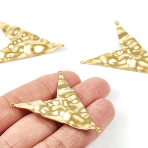 May include: Gold-colored, textured metal triangle charms with a hammered finish. The charms have a small loop at each point for attaching to jewelry. One charm is held in a hand, with two others on a white background.