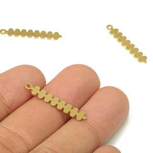 May include: Gold-coloured metal charm featuring a series of connected flower-shaped cutouts. The charm has a small loop at one end for attaching to jewellery. Several charms are visible against a white background.