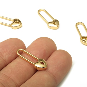 Peut inclure: Charm en forme d'épingle à nourrice dorée en forme de cœur. Les breloques ont un design de serrure en forme de cœur avec un trou de serrure. L'épingle à nourrice est de conception classique, avec un dessus incurvé et une épingle droite. Les breloques sont petites et délicates.