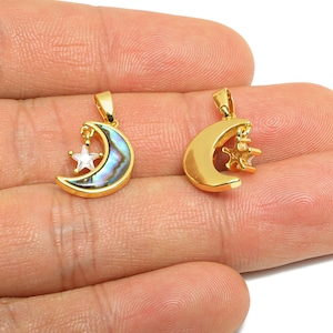 Pode incluir: Dois pingentes de lua dourados com detalhes de estrela. Um pingente apresenta uma lua crescente com incrustações de concha de abalone e uma estrela transparente. O outro tem uma lua crescente e uma estrela douradas. Os pingentes são pequenos e delicados.