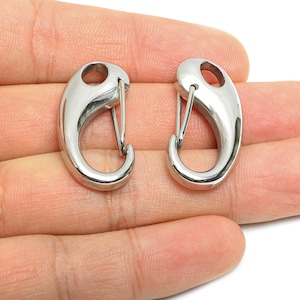 Op de afbeelding: Twee gepolijste, zilverkleurige karabijnhaakclips. Elke clip heeft een gebogen behuizing met een veergeladen poort. De clips worden getoond tegen een neutrale achtergrond, wat het ontwerp en de functionaliteit van het product benadrukt. Deze worden waarschijnlijk gebruikt voor het vastzetten van items.