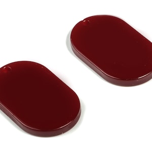 Puede incluir: Dos abalorios ovalados de color rojo con un agujero en la parte superior.