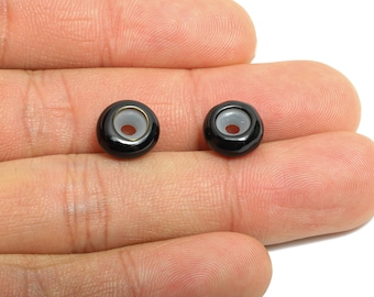 May include: Two black ceramic beads with a light gray center and a gold-colored rim. The beads are round with a hole through the center. These beads are suitable for jewelry making and other craft projects.