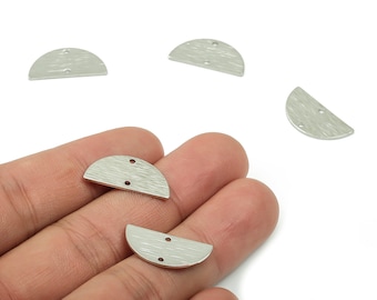 May include: Silver-toned, half-moon shaped metal jewelry findings with a textured surface and two small holes. Several pieces are scattered, with some held in a hand. These components are ideal for crafting earrings, pendants, or other jewelry.