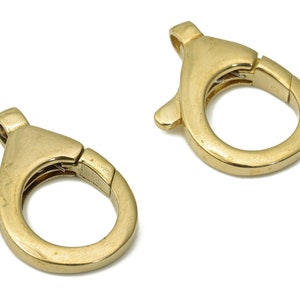 Puede incluir: Dos cierres de langosta de metal dorado, cada uno con una abertura de resorte y un diseño liso y redondeado.