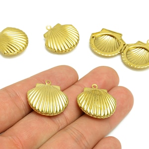 May include: Gold-colored seashell-shaped pendants with a hinged design. The pendants have a textured, ridged surface and a small loop for attaching to a chain or other jewelry component. One pendant is open, revealing the interior.