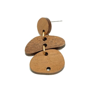 May include: A single wooden earring with a post, featuring a circular top and three irregularly shaped, connected wooden pieces. The earring is a warm brown color, with gold-colored connecting rings. The background is plain white.