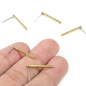 Op de afbeelding: Een verzameling goudkleurige staafvormige oorstekers met zilveren pinnen. De oorbellen zijn rechthoekig en hebben een minimalistisch ontwerp. De afbeelding is genomen op een witte achtergrond.