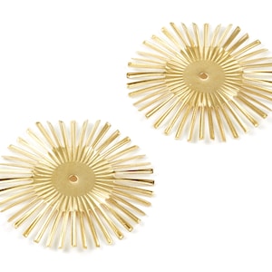 May include: Two gold-colored metal sunburst shapes with a circular center hole. The sunburst shapes are made of thin metal strips radiating out from the center.