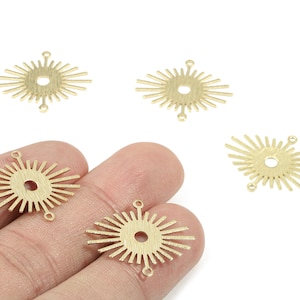 May include: Gold-colored sunburst charms with a central hole and radiating lines. Each charm has three small loops for attaching to jewelry. The charms are shown on a white background and held by a hand.