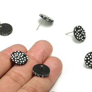 May include: A collection of black and white polka dot stud earrings. The earrings are circular, with a black base and white spots. The image is set against a white backdrop.