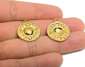 May include: Two gold-colored round pendants with a celestial design. Each pendant features a central oval shape surrounded by crescent moon shapes and small circles. The pendants have a loop at the top for attaching to a chain or other jewelry.