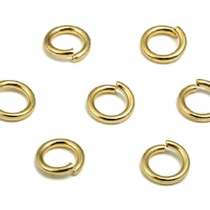 Op de afbeelding: Zeven gouden springringen, ook wel splitringen genoemd, zijn in een cirkelvormige opstelling op een witte achtergrond geplaatst. Deze ringen worden vaak gebruikt bij het maken van sieraden en handwerk.