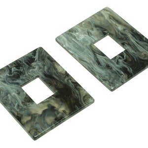 Puede incluir: Dos pendientes de forma cuadrada con un patrón de mármol en tonos de negro, blanco y gris. Cada pendiente tiene un agujero rectangular en el centro.