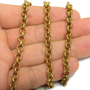May include: Close-up of three strands of a gold-colored chain. The chain links are textured and connected in a repeating pattern. The chain is held in a person's hand.